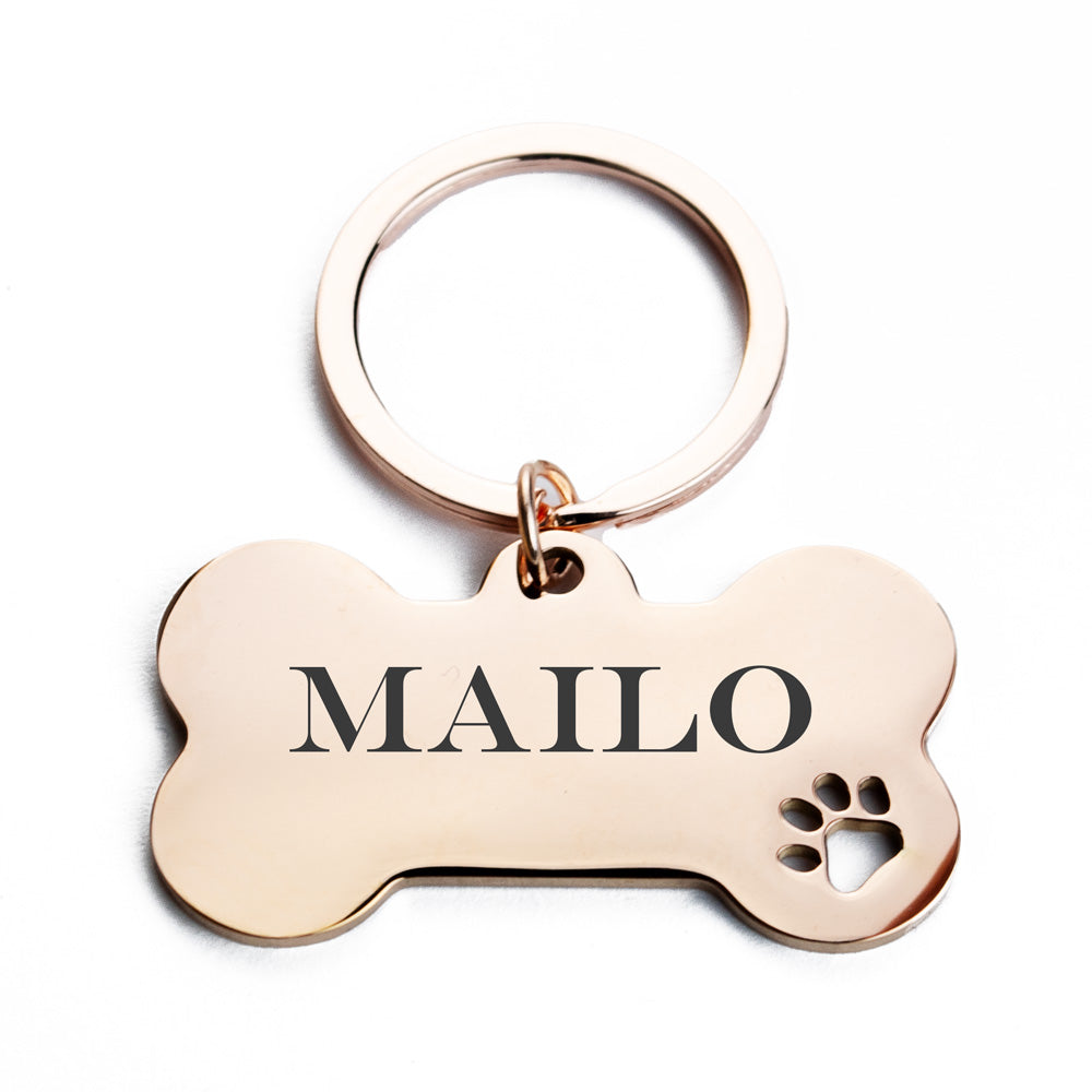 Die Abbildung zeigt ein Hundemarkenanhänger in Form eines Knochens, der an einem Schlüsselring befestigt ist. Auf dem Anhänger ist der Name “MAILO” eingraviert, und darunter befindet sich eine Pfotenabdruck-Gravur. Der Schlüsselring ist kreisförmig und besteht ebenfalls aus Edelstahl.